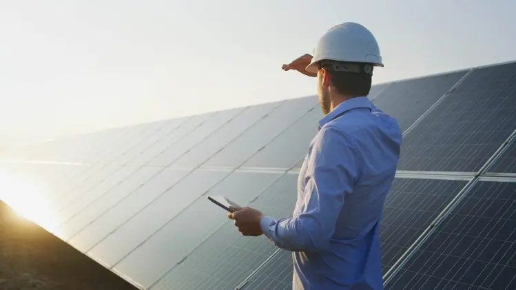 An young engineer is checking with tablet an operation of sun and cleanliness on field of photovoltaic solar panels on a sunset. Concept:renewable energy, technology,electricity,service, green,future